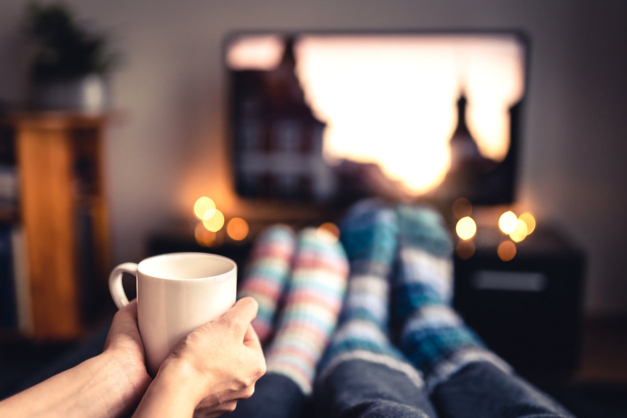 Couple drinking tea, hot chocolate, eggnog or mulled wine and watching tv in warm cozy woolen socks in winter. Woman holding cup of morning coffee in home living room. Sick people with flu. Couple drinking tea, hot chocolate, eggnog or mulled wine and watching tv in warm cozy woolen socks in winter. Woman holding cup of morning coffee in home living room. Sick people with flu.