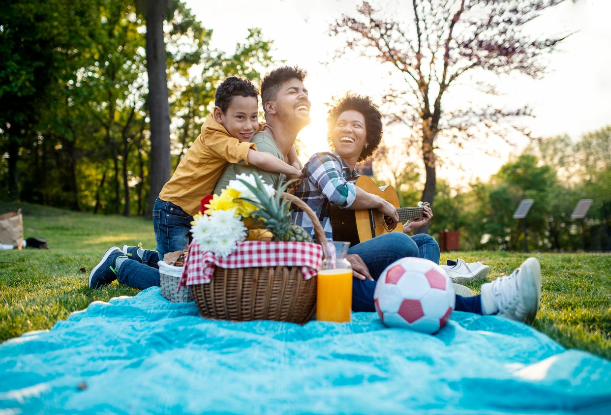 Happy family play guitar and sing together while sitting in the park in summer. Happy family play guitar and sing together while sitting in the park in summer.